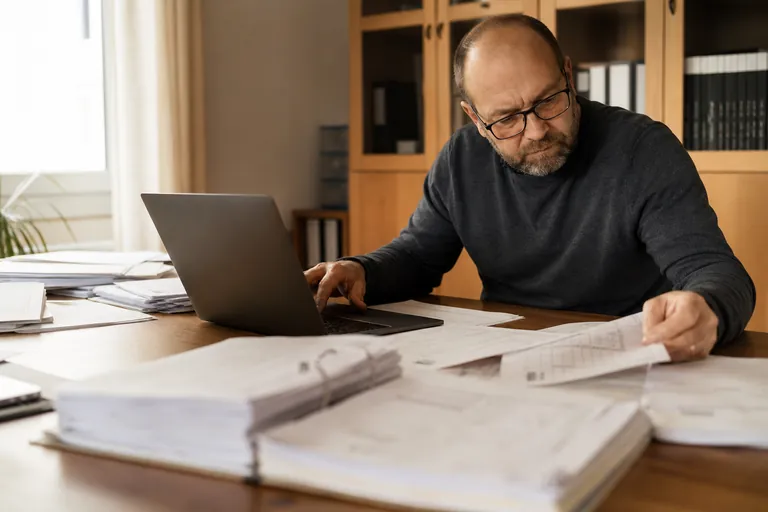 Vermieter erstellt mit Laptop und Abrechnungsunterlagen eine Betriebskostenabrechnung.