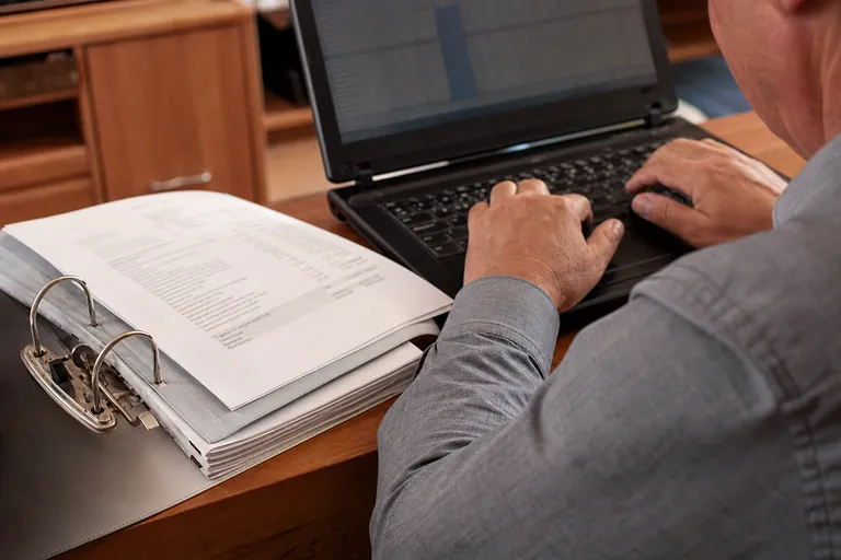 Vermieter vergleicht Tabellenarbeit am Laptop mit abgelegten Abrechnungsunterlagen.